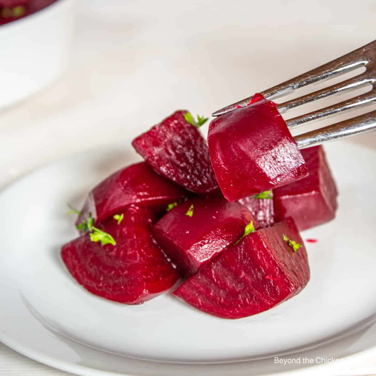 Cooked beets on a plate with a fork in one beet.