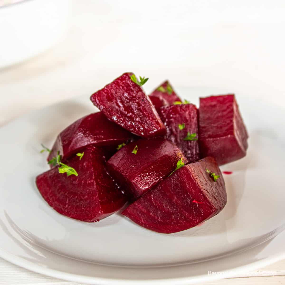 Cubed beets topped with fresh parsley on a white plate.
