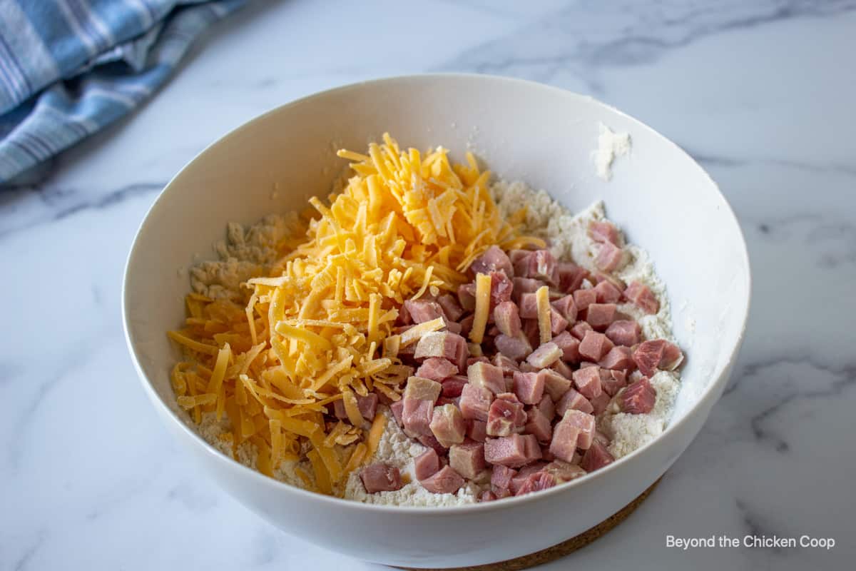 Shredded cheddar cheese and small cubed ham in a white bowl.