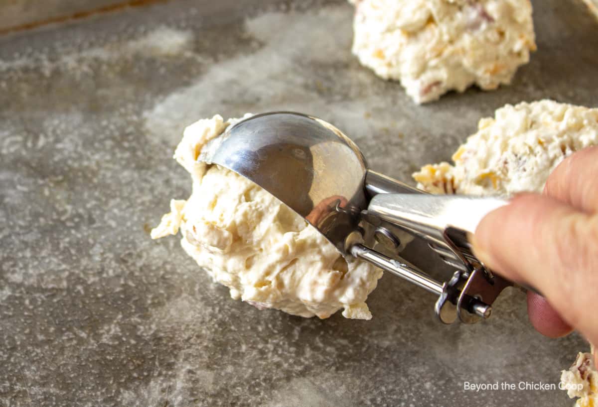Biscuit dough being dropped onto a baking sheet with an ice cream scoop.