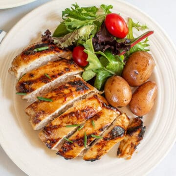 Grilled and sliced chicken breast on a plate with salad and potatoes.