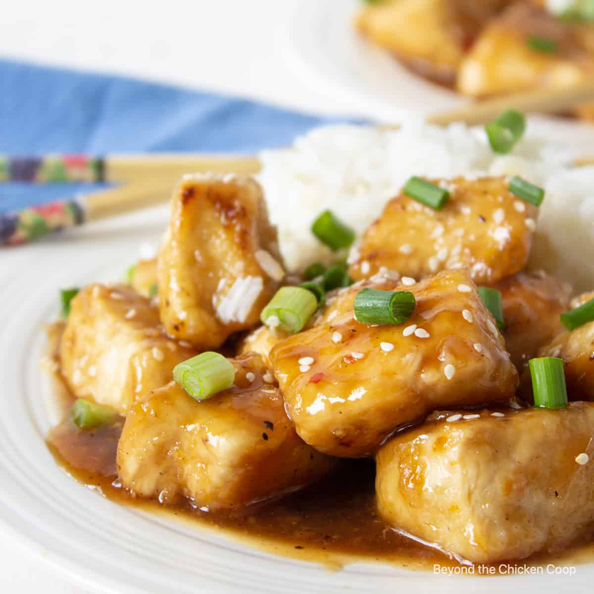 Cubes of chicken covered in an orange sauce on a white plate.