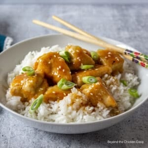 A white bowl filled with orange chicken with rice.