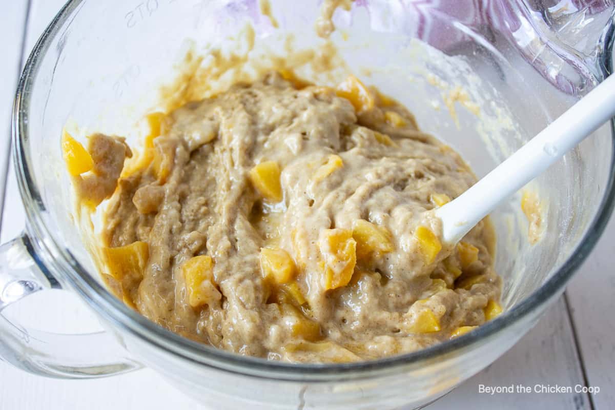 Peaches in a muffin batter in a glass bowl.