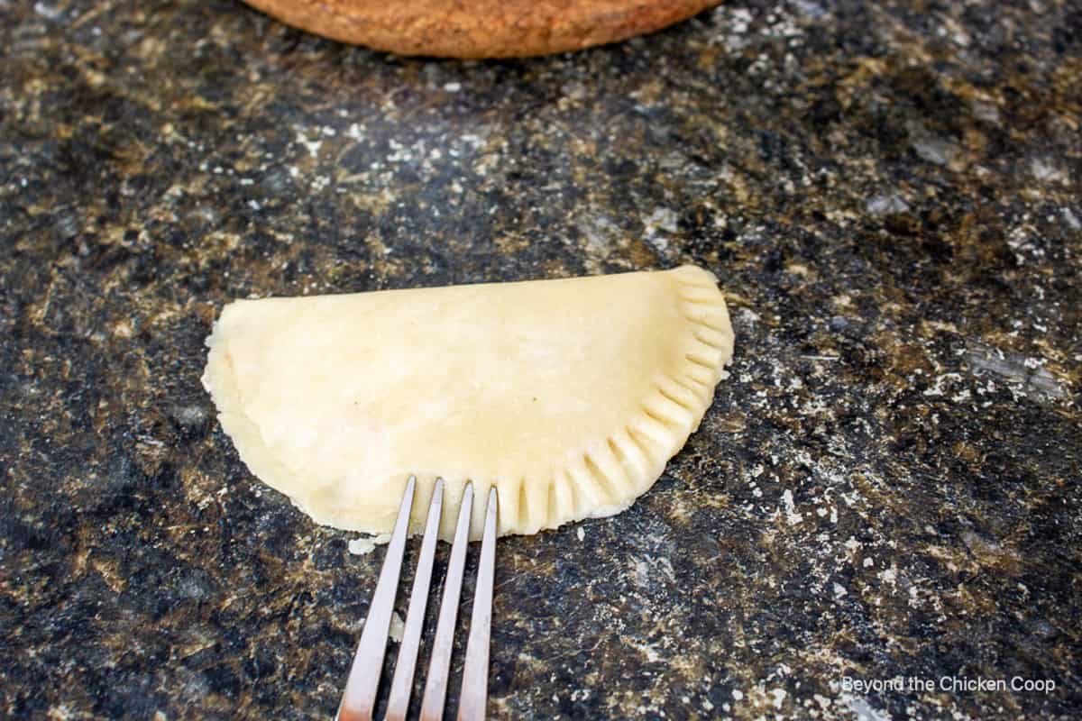A half moon shaped pie dough being crimped with a fork.