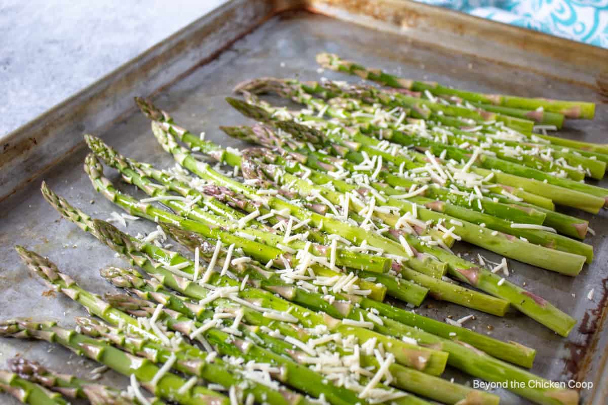 Asparagus topped with parmesan cheese on a baking sheet.