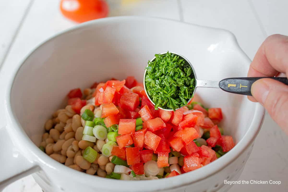 A tablespoon of chopped parsley above a bowl with a bean salad.