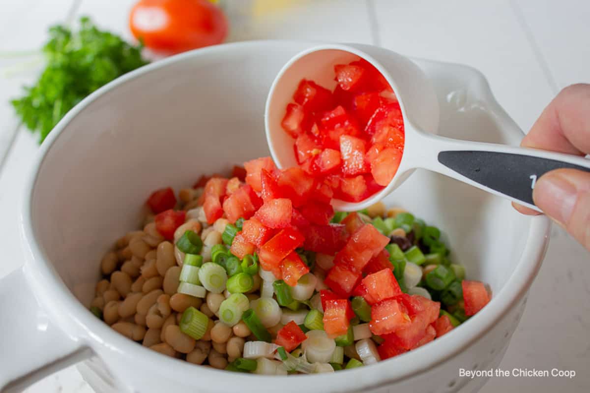 Chopped tomatoes being added to a bowl full of beans.