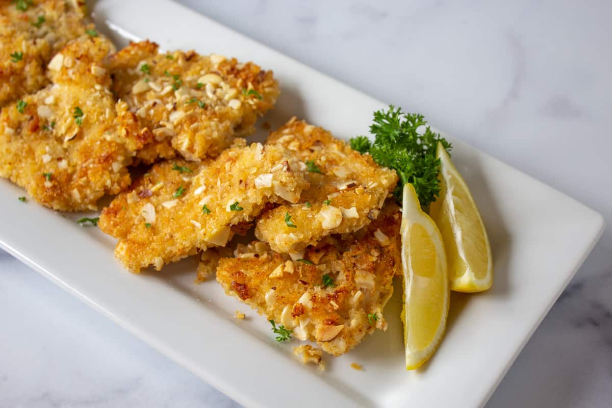 Almond crusted fish fillets on a platter with lemon wedges. 