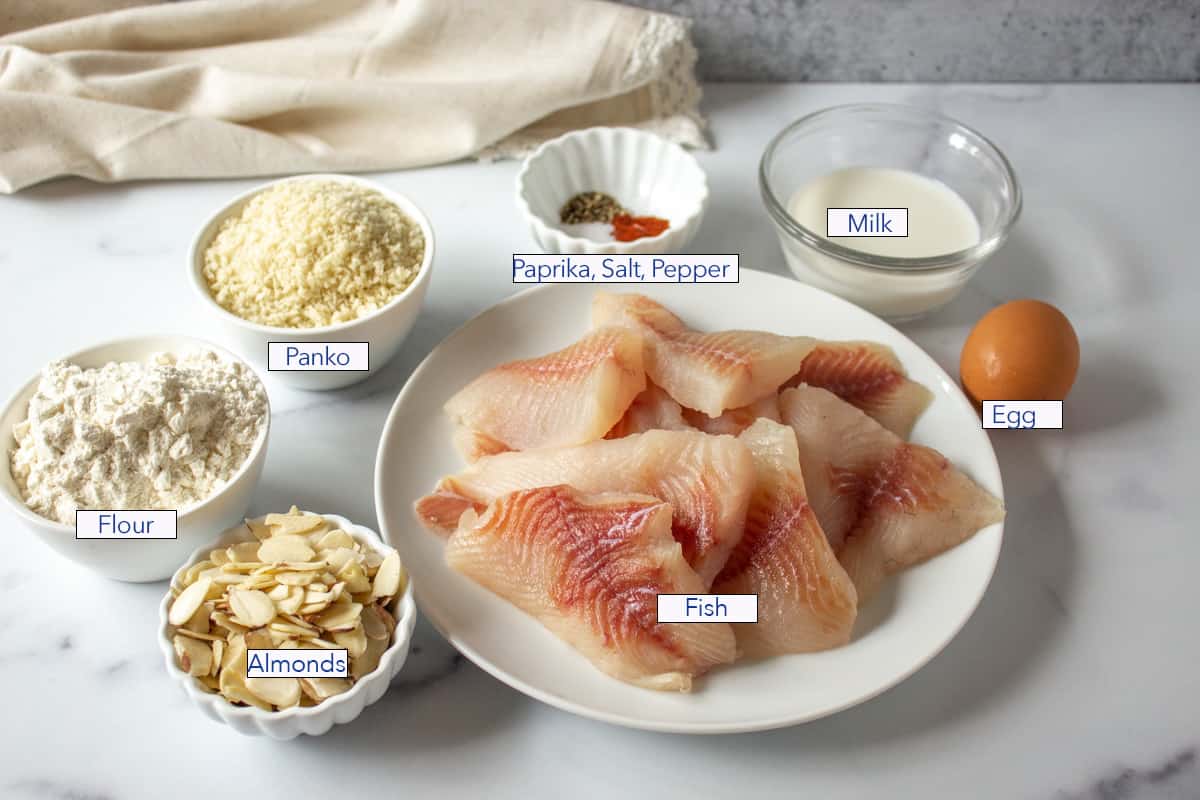 A plate with uncooked fish fillets and small bowls filled with almonds, flour and panko.