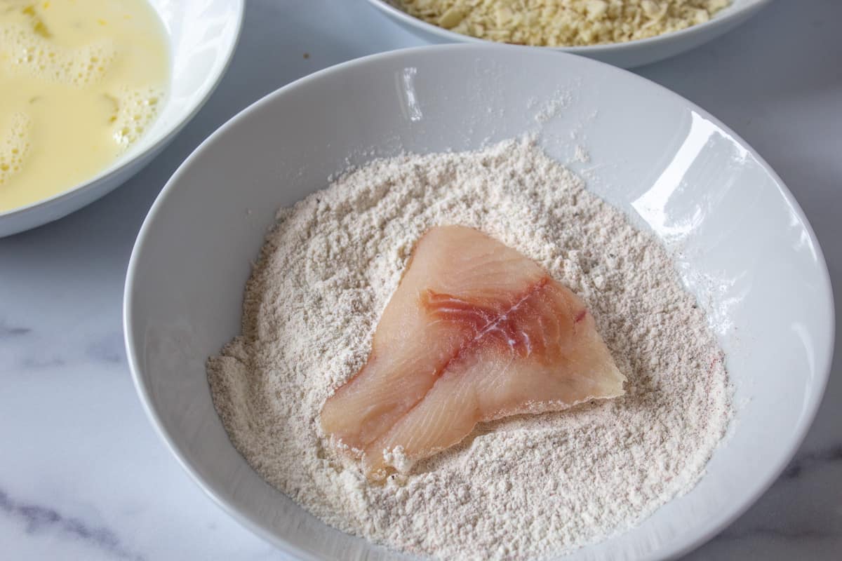 A fish fillet in a bowl of flour. 