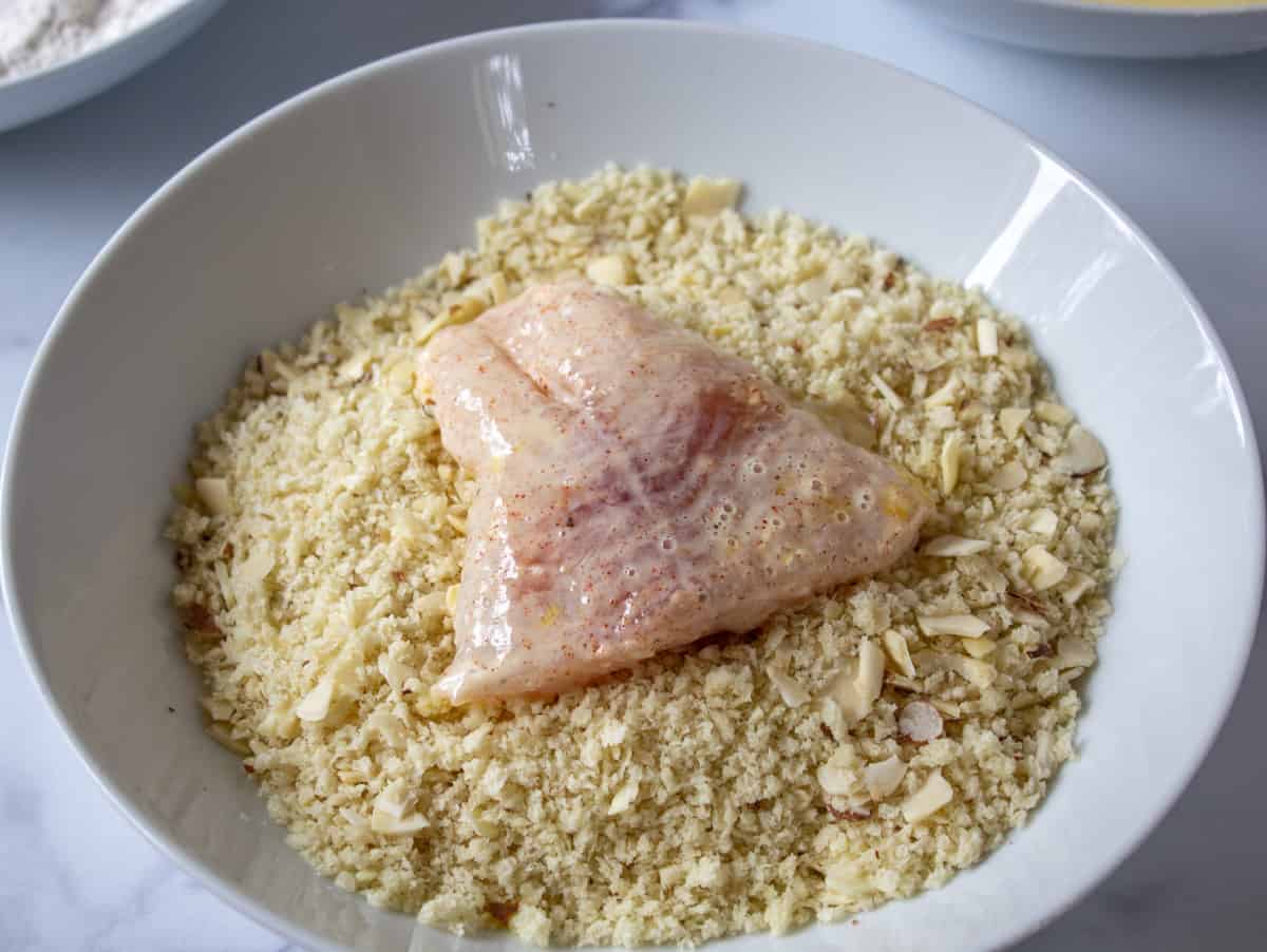 A fish fillet in a bowl with panko bread crumbs.