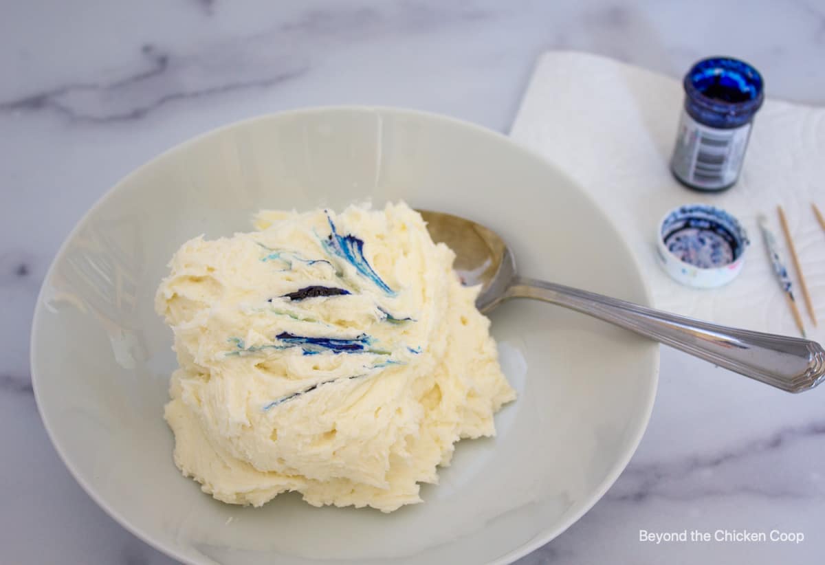 A bowl of white frosting with streaks of blue coloring across the top.