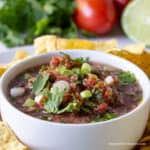 A white bowl filled with a tomato salsa with green onions and cilantro.