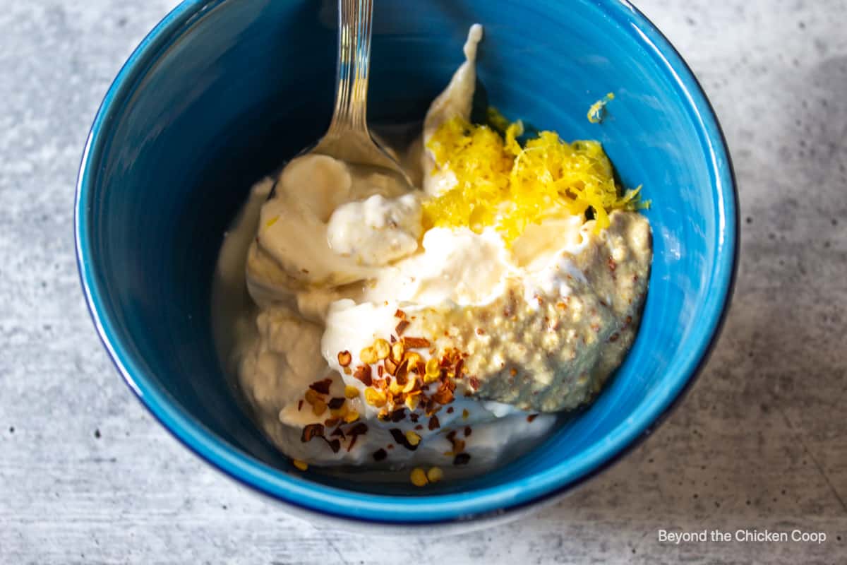 A blue bowl filled with mayonnaise, mustard and seasonings.