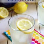 A glass filled with lemonade with a slice of a lemon floating on the top.