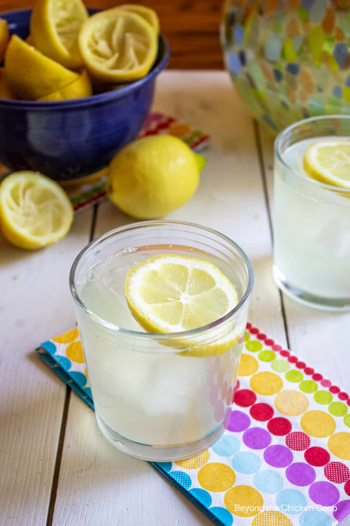 A glass of lemonade and a bowlful of lemons on a white board. 