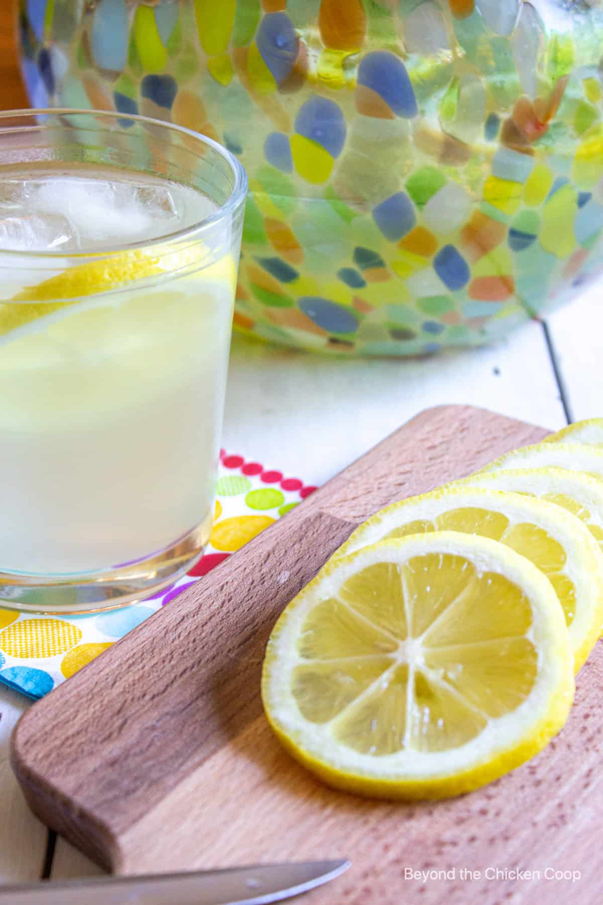 Lemon slices on a cutting board next to a glass of lemonade.