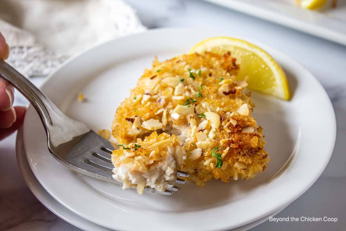 A cooked fish fillet on a plate with a fork.