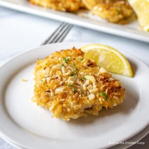 A fish fillet coated with bread crumbs and crushed almonds on a white plate.