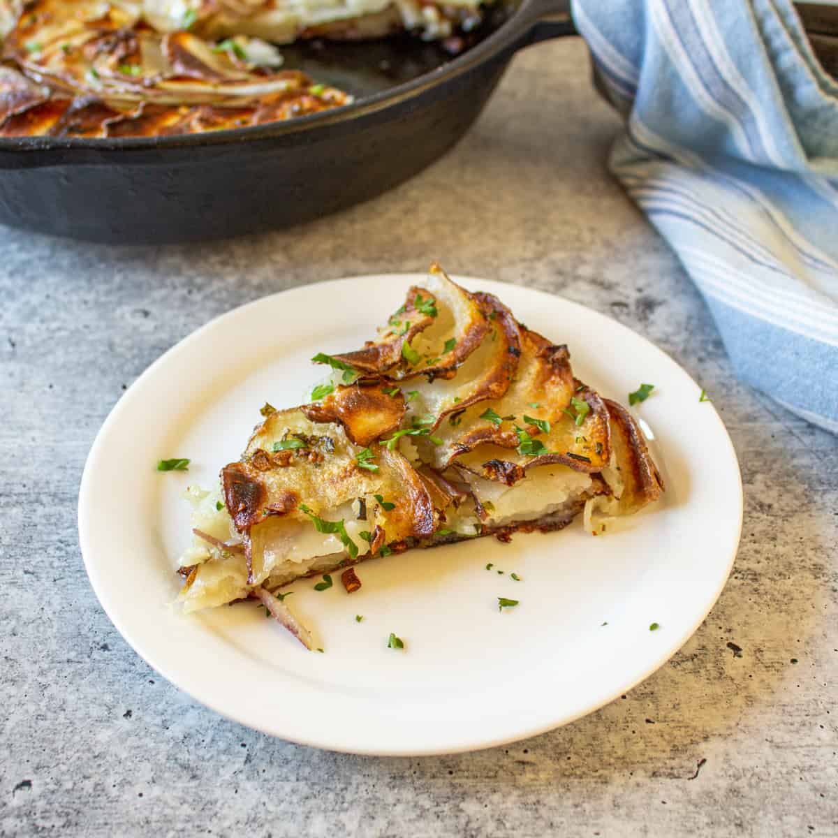 A round white plate topped with a wedge of a potato galette.