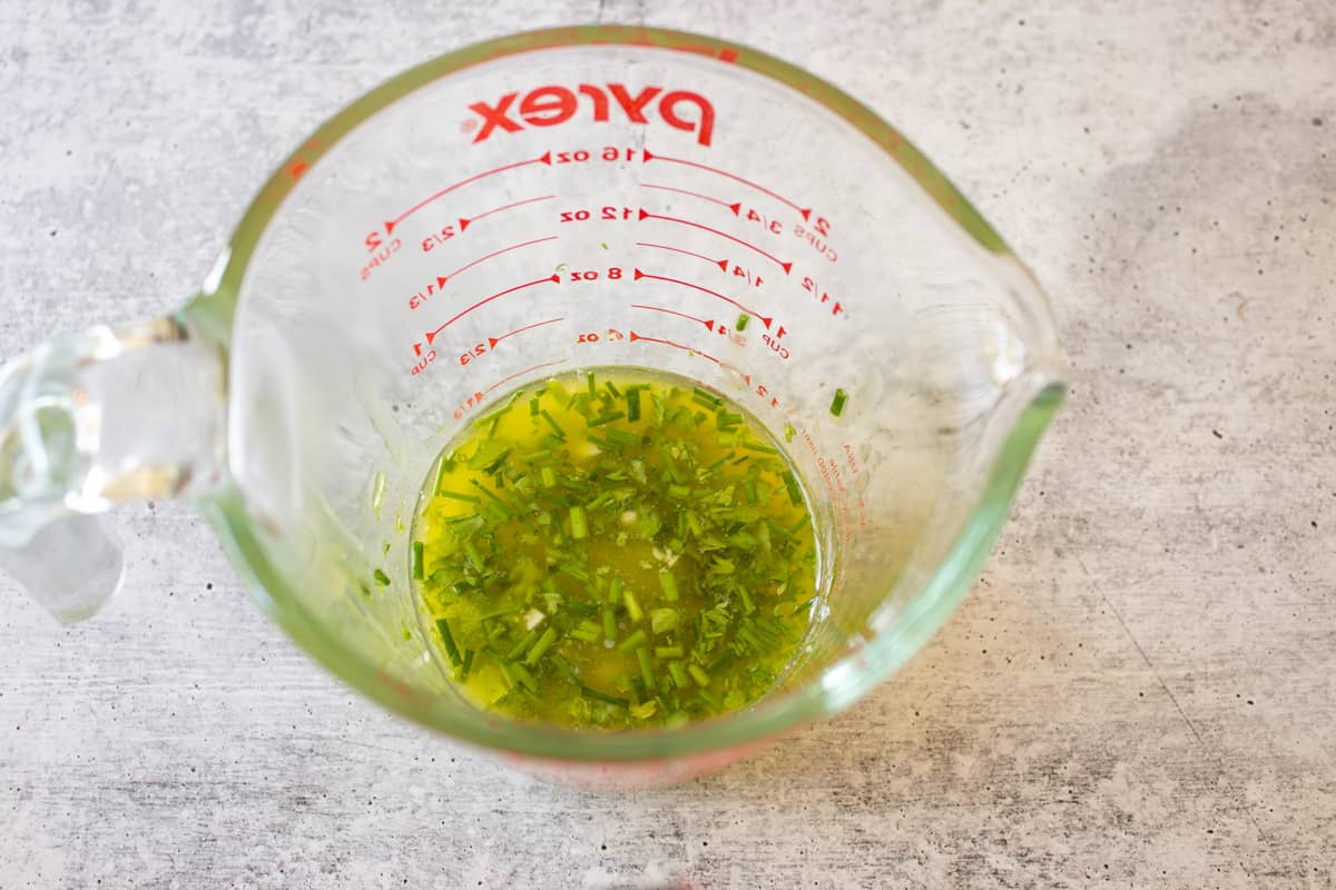 A measuring dish with melted butter and fresh herbs and garlic.