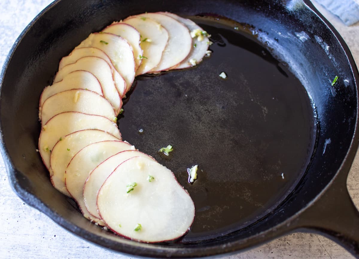 Sliced potatoes in a concentric overlapping circle in a black skillet