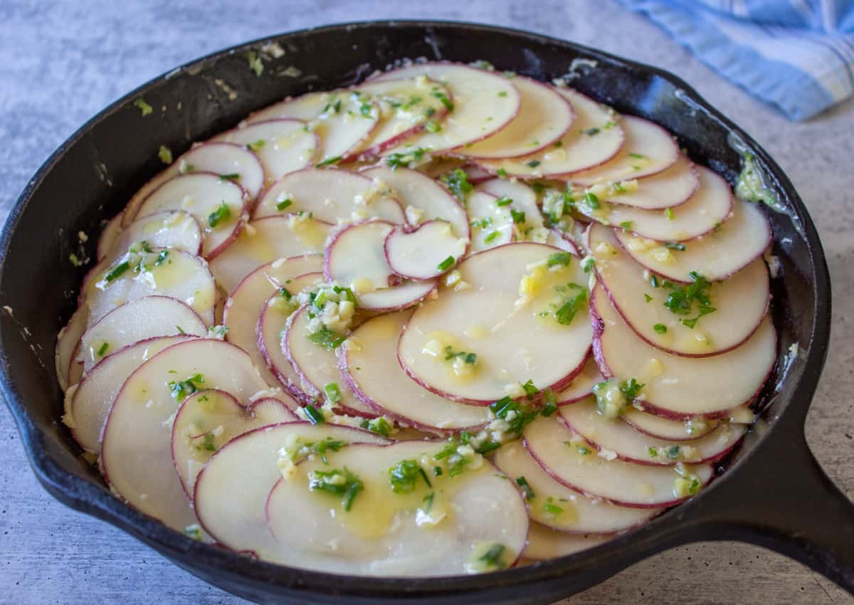 An unbaked potato dish in a black cast iron skillet.