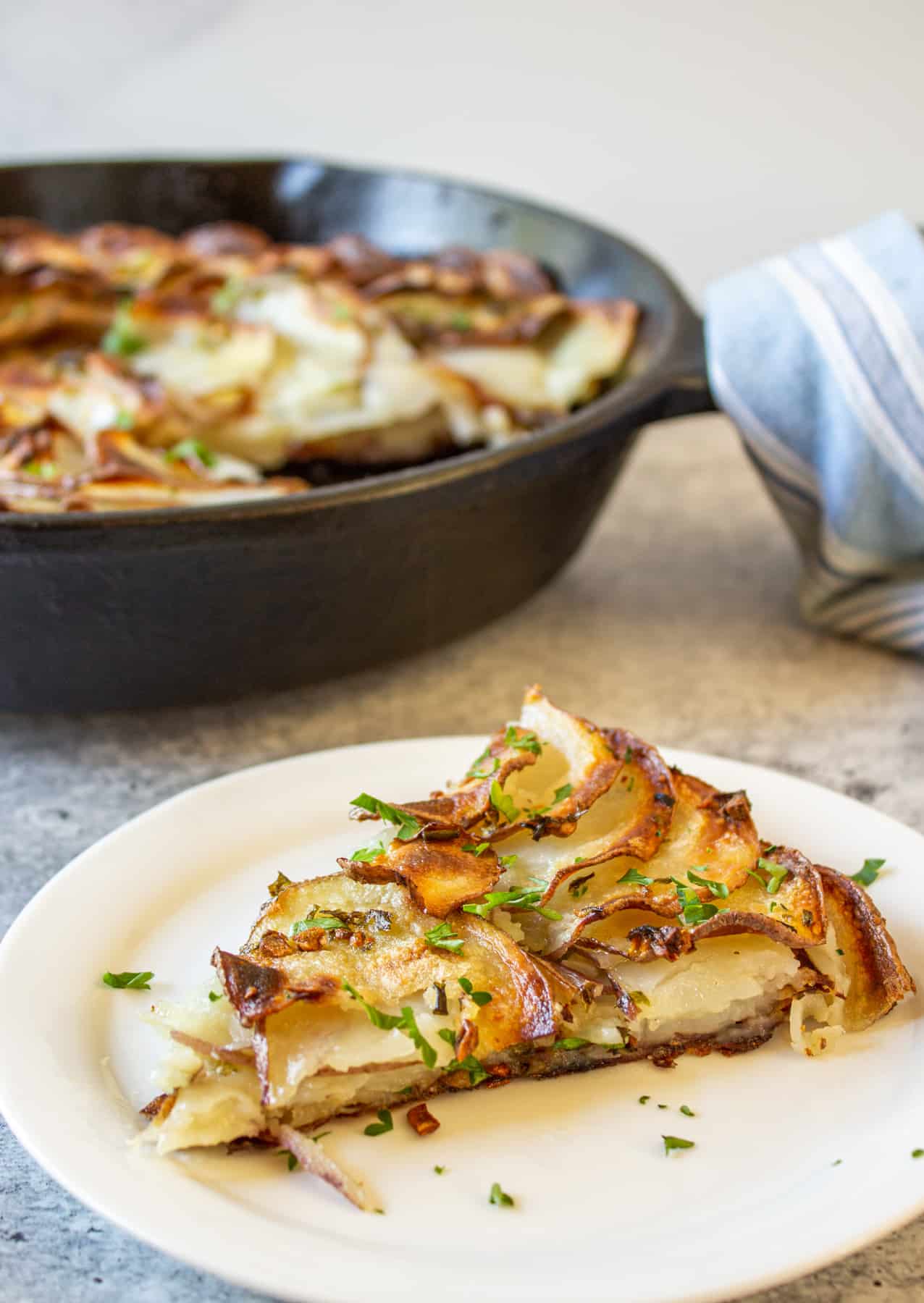 A sliced potato dish topped with fresh parsley on a white plate.