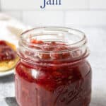 A glass canning jar filled with a dark red jam.