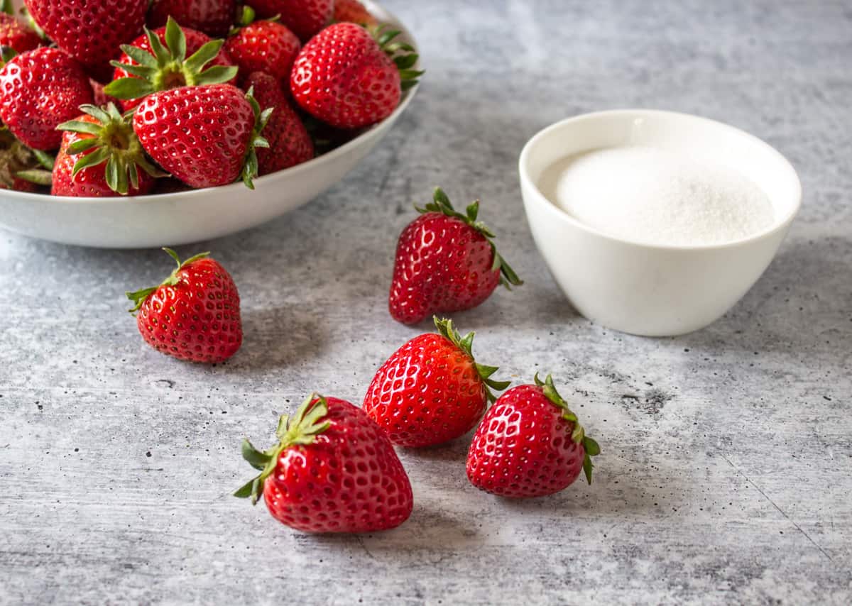 Fresh strawberries on a counter next to a small bowl of sugar.