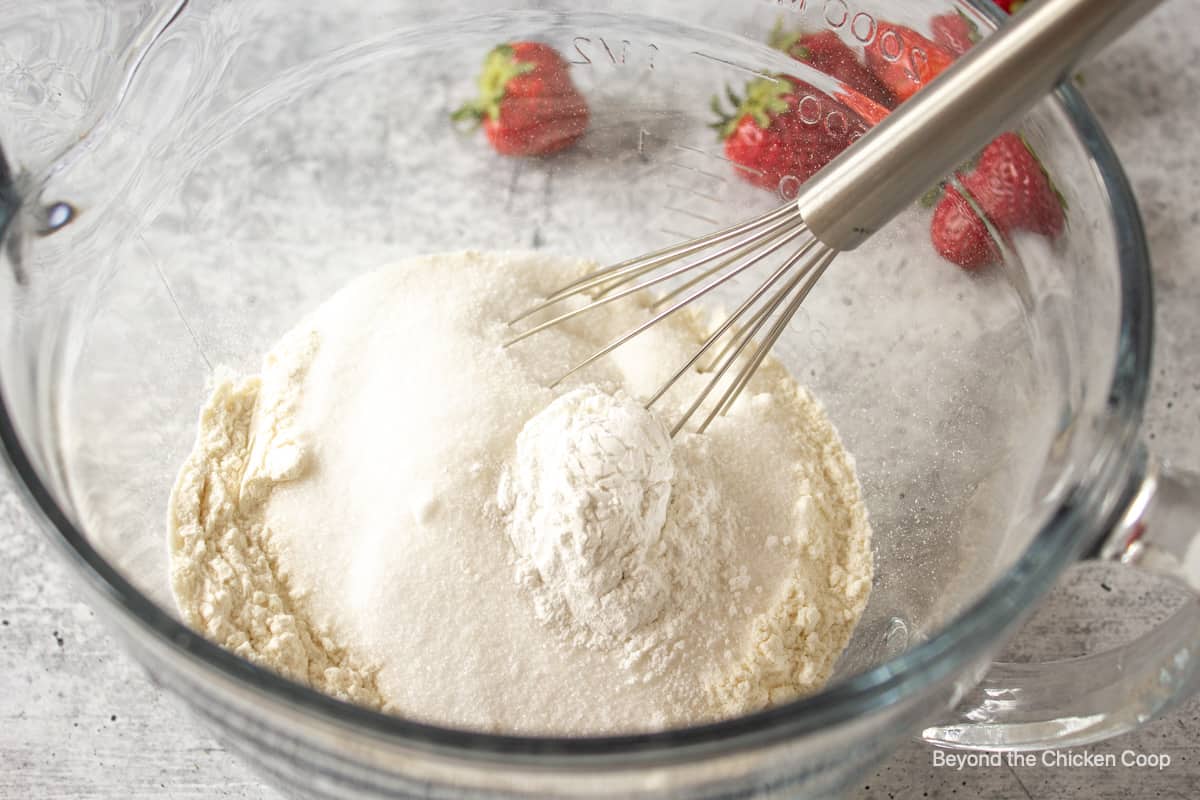 A bowl filled with flour and sugar with a whisk in the middle of the flour. 