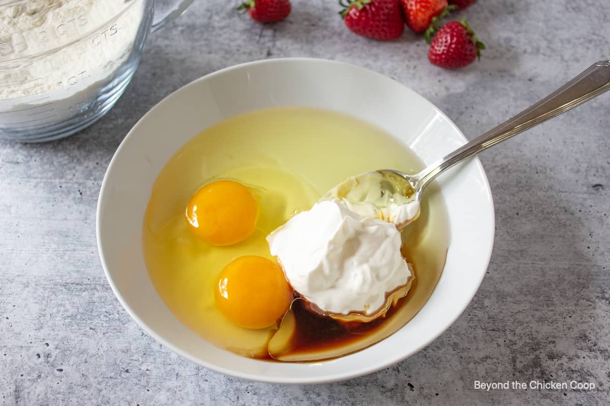 A white bowl with eggs, sour cream, oil and vanilla.