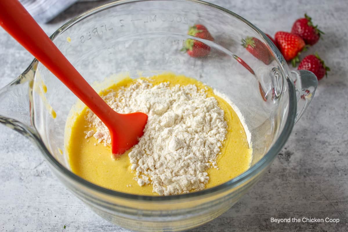 Muffin batter being mixed in a glass bowl with a spatula.