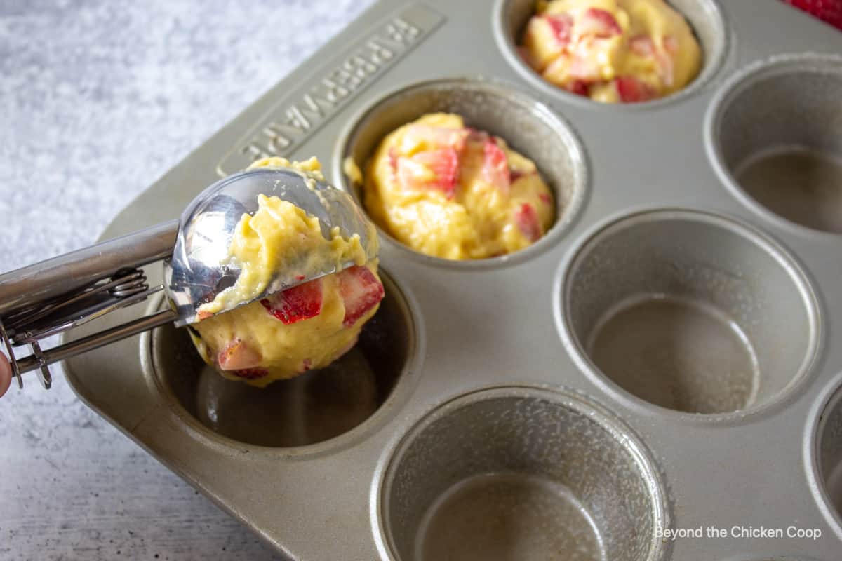 Muffin batter being scooped into a muffin tin.