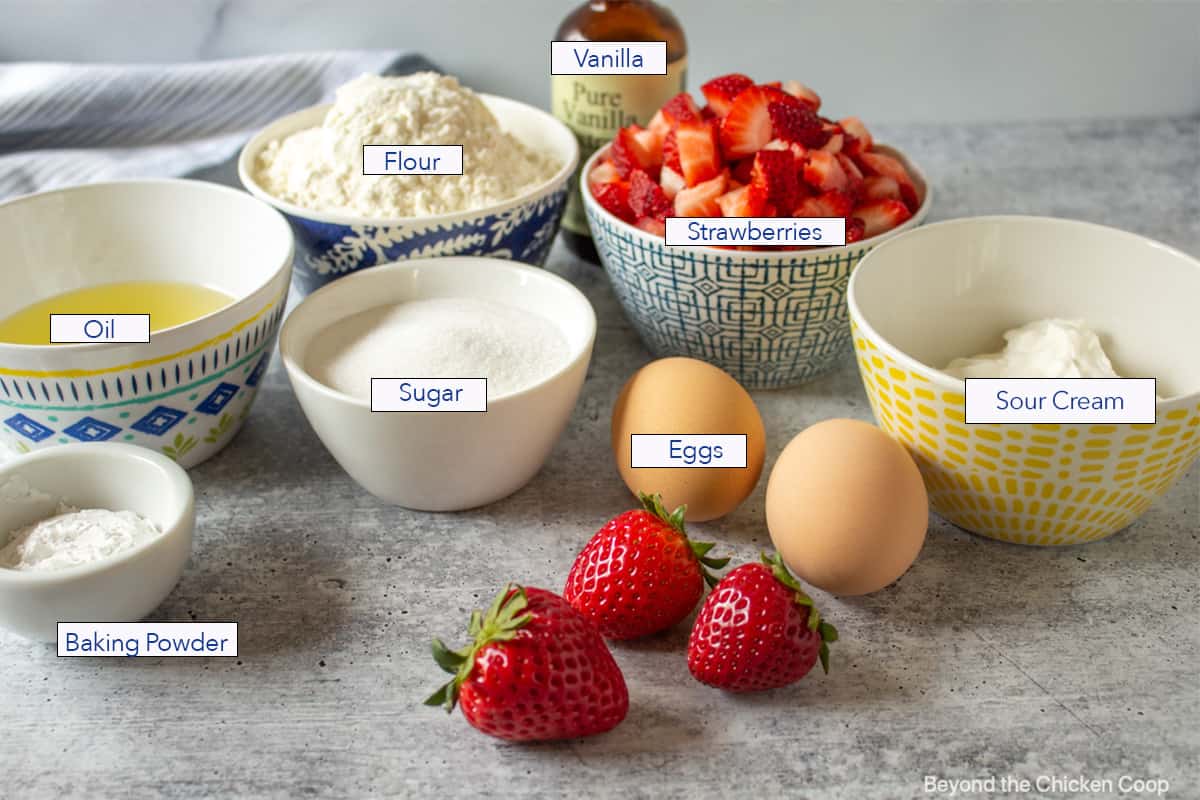 Fresh strawberries along with small bowls of ingredients for making muffins. 