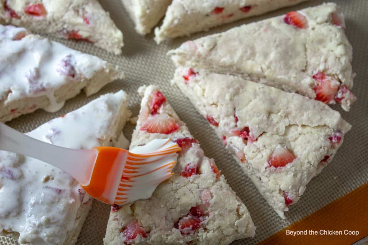 Brushing cream on top of unbaked scones.