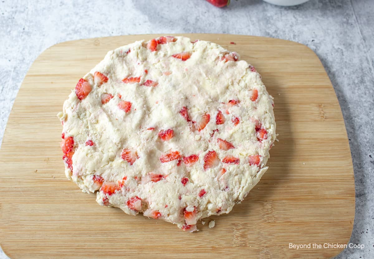 A round of scone dough on a wooden cutting board.