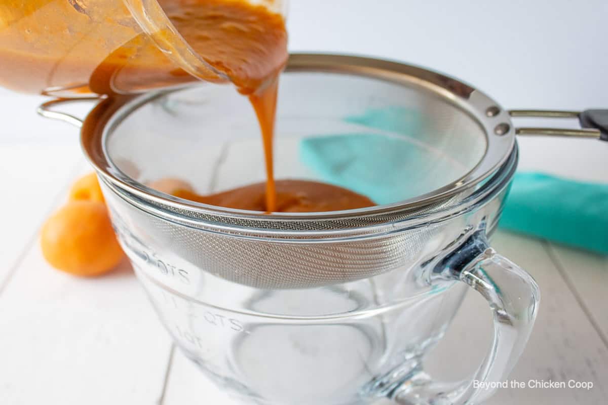 An apricot puree being poured through a sieve.