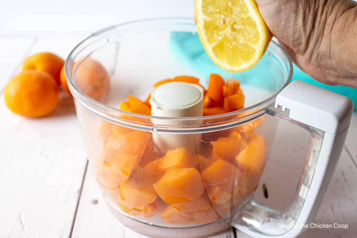 A fresh lemon being squeezed over cut apricots.