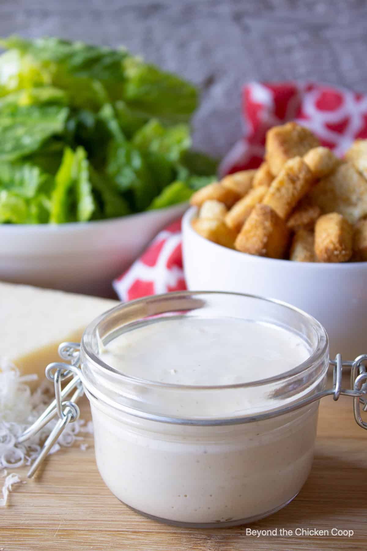 A jar filled with a creamy dressing with salad ingredients in the background