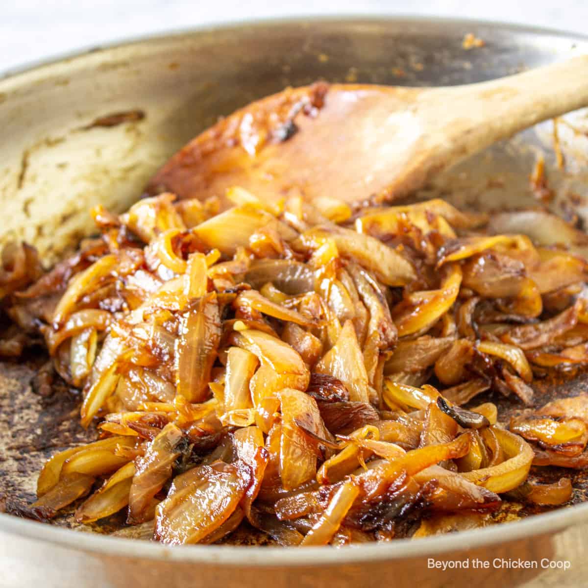 Caramelized onions in a fry pan with a wooden spoon.