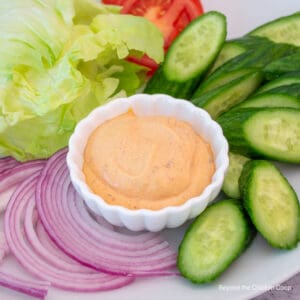 A small dish filled with chipotle mayonnaise surrounded by veggies.