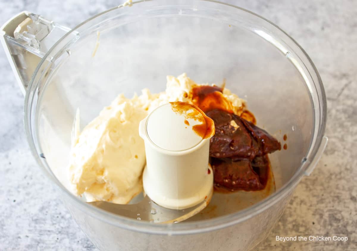 A food processor with mayo and peppers in the bowl.