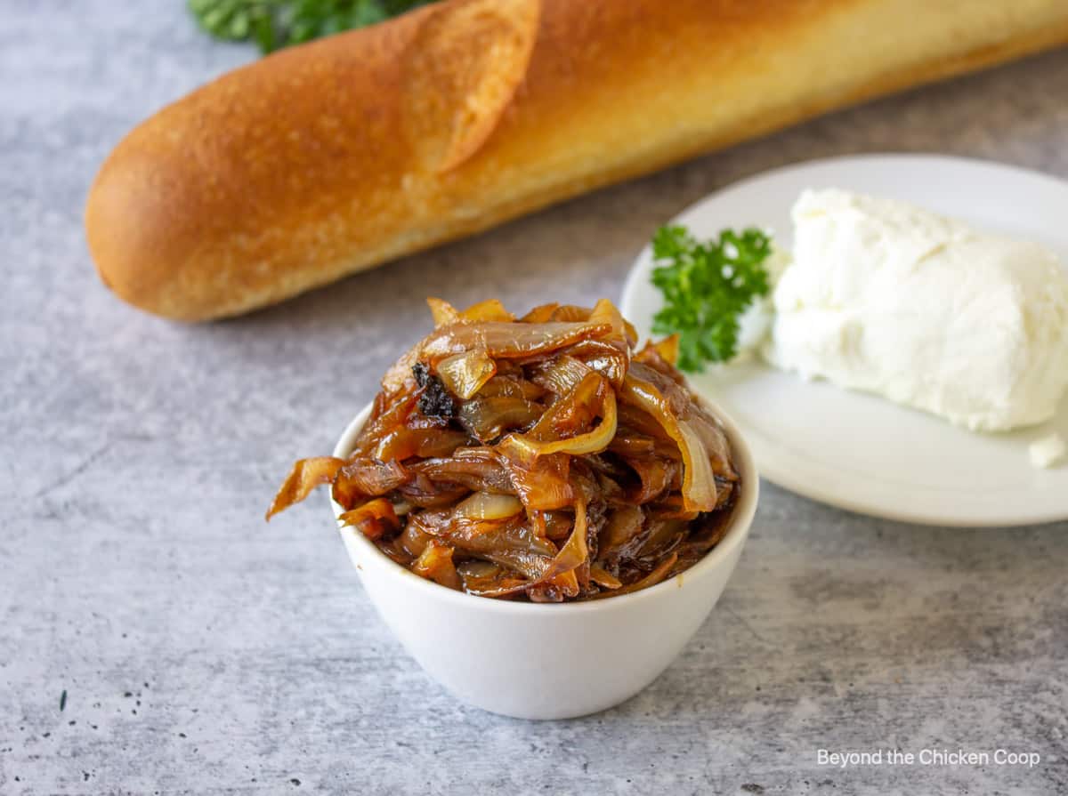 Caramelized onions in a small bowl next to a log of goat cheese and a loaf of bread.