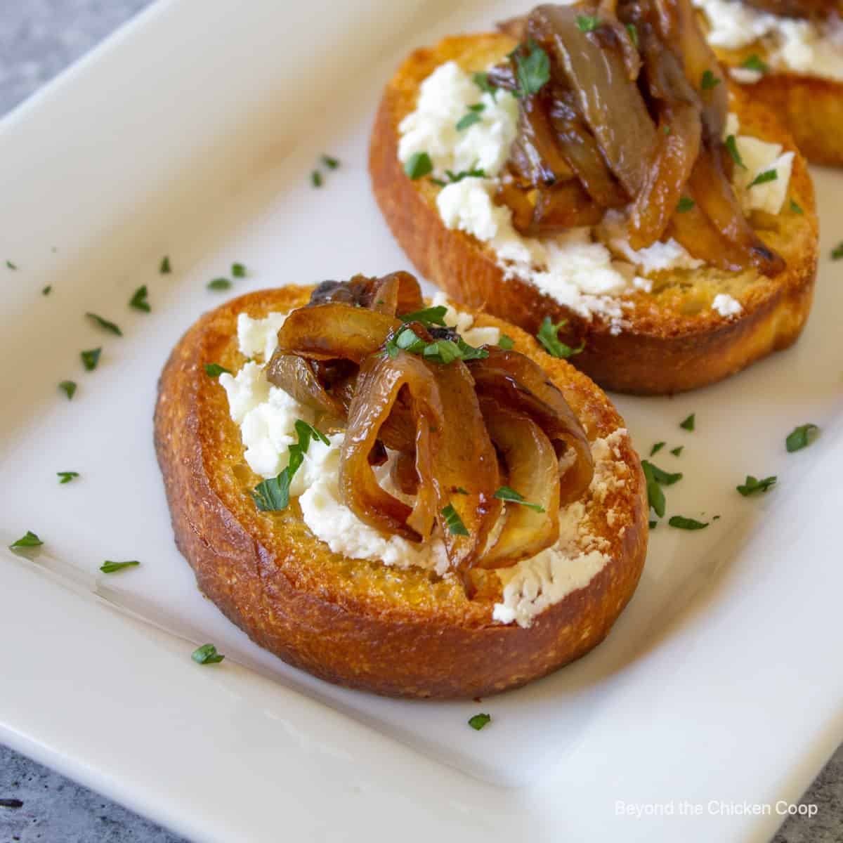Crostini topped with goat cheese and caramelized onions on a platter.