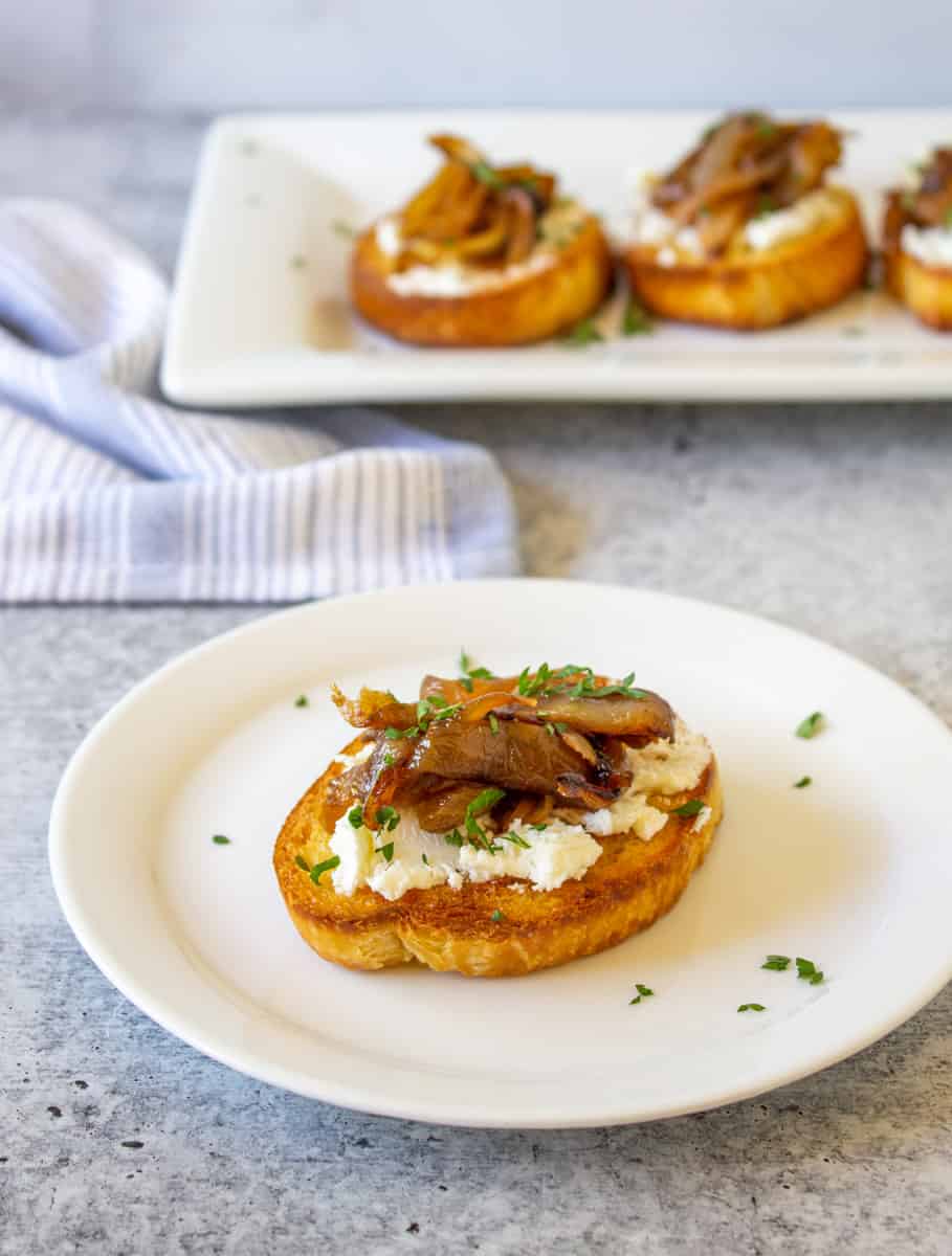 A crostini with cheese and onions on a white plate.