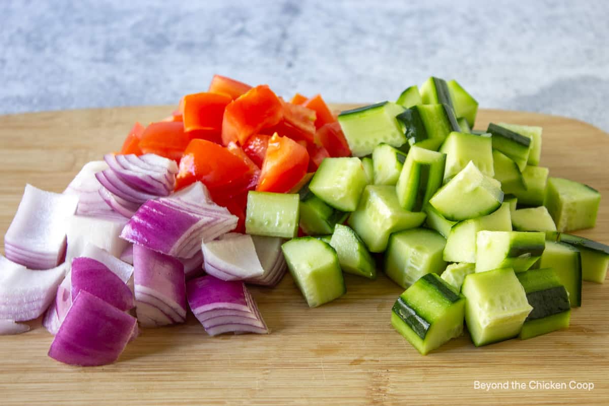 Chopped onions, tomatoes and cucumbers on a wooden board.