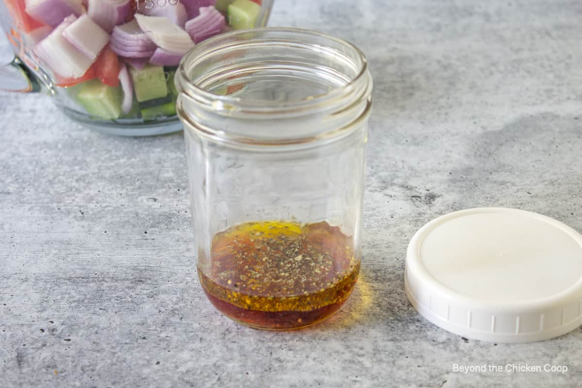 A glass jar filled with oil, vinegar and dried herbs.