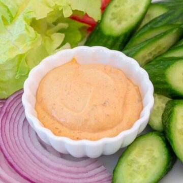 A small bowl filled with a dip with fresh veggies around the bowl.